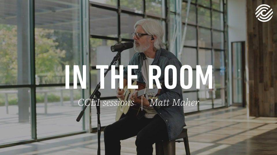 Matt Maher performing with a guitar and microphone in open modern space