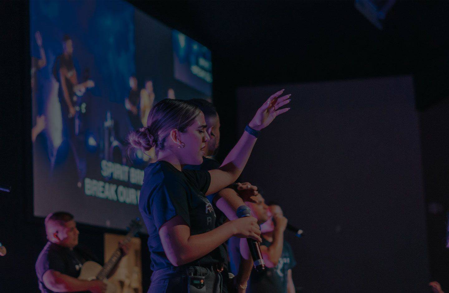 Profile shot of worship team leading worship on stage with lyrics displayed behind them.