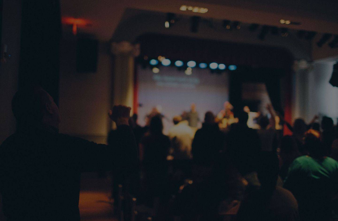 Adoración en la Iglesia donde las personas están de pie en una habitación mirando hacia un escenario iluminado.