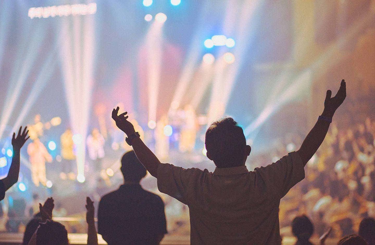 Picture of a worshipper with arms raised in a large Korean church service