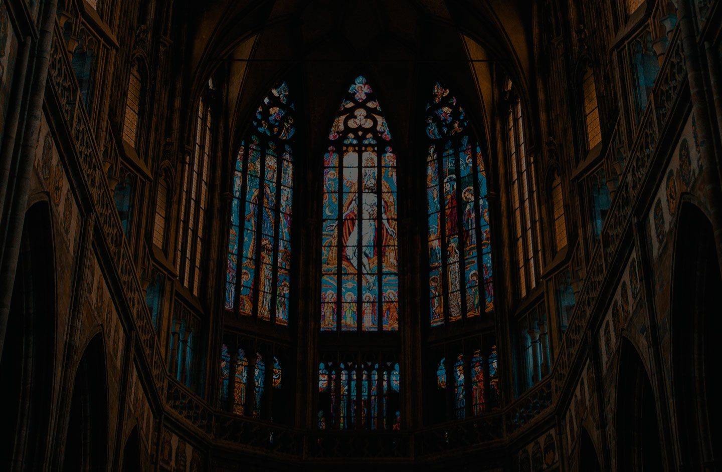 Tall walls reaching up towards the ceiling of an old cathedral. Colorful stained-glass windows portraying religious artwork.